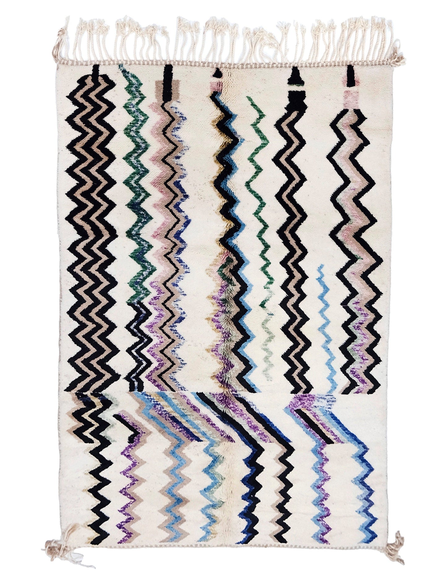 A plush cream-colored Moroccan Azilal shag rug featuring vibrant, hand-woven vertical zigzag lines in black, teal, purple, and blue, with white fringe detailing on the top edge and corner tassels at the bottom.