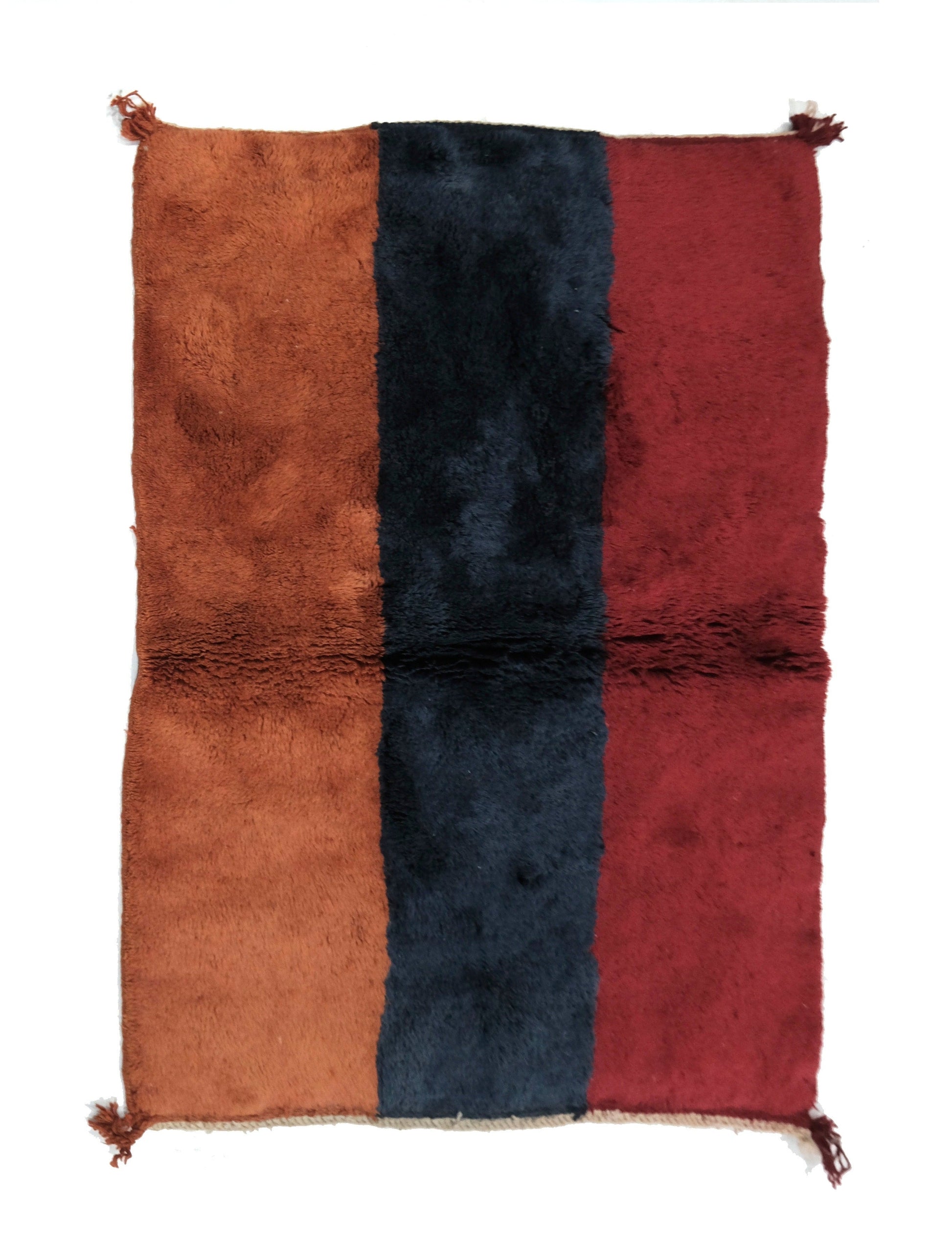 Plush hand-loomed wool rug featuring three wide vertical stripes in terracotta rust, navy blue, and deep burgundy red, with a horizontal central joining seam and small corner tassels, displayed on a white background