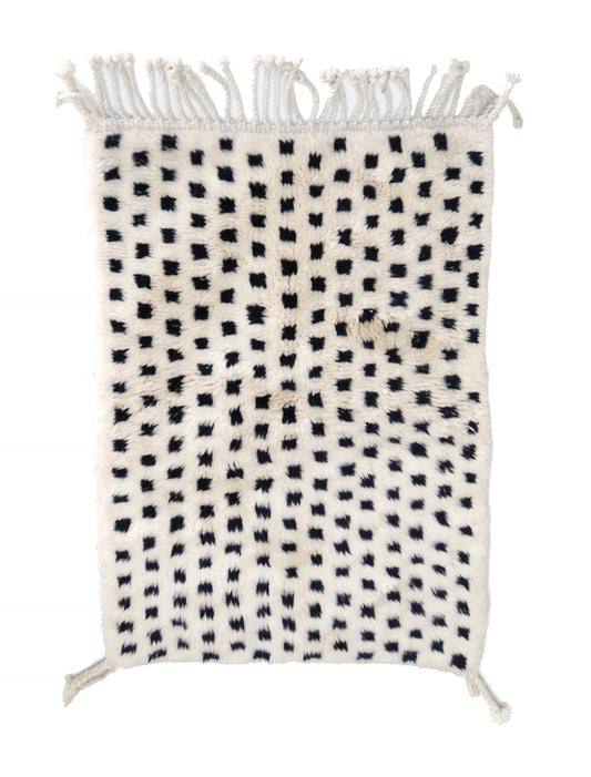 Plush cream wool rug with a grid of raised, fuzzy black tufted dots, featuring a chunky twisted top fringe and small braided corner ties, displayed on a white background.

