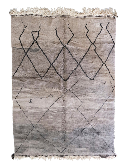 Muted grey plush handwoven Moroccan wool rug featuring a dark central joining seam, a "stepped" or broken black diamond lattice pattern, small scattered tribal motifs in the lower area, and cream fringe at the top and bottom, displayed on a white background.