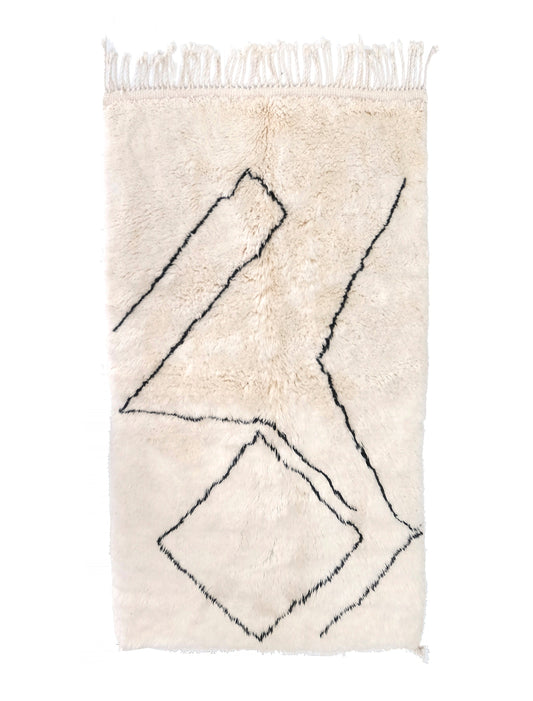 Plush cream wool rug featuring an abstract pattern of black hand-drawn angular lines and a broken diamond shape, with a knotted top fringe and a small bottom corner tie, displayed on a white background.