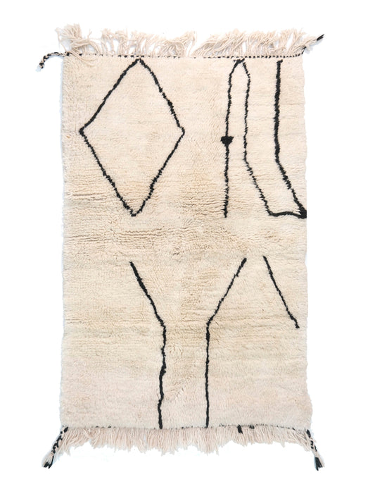 A cream-colored handwoven Moroccan shag rug featuring minimalist black line art, including a large diamond shape, vertical wavy lines, and Y-shaped branches, with cream fringe and black corner accents on the edges.

