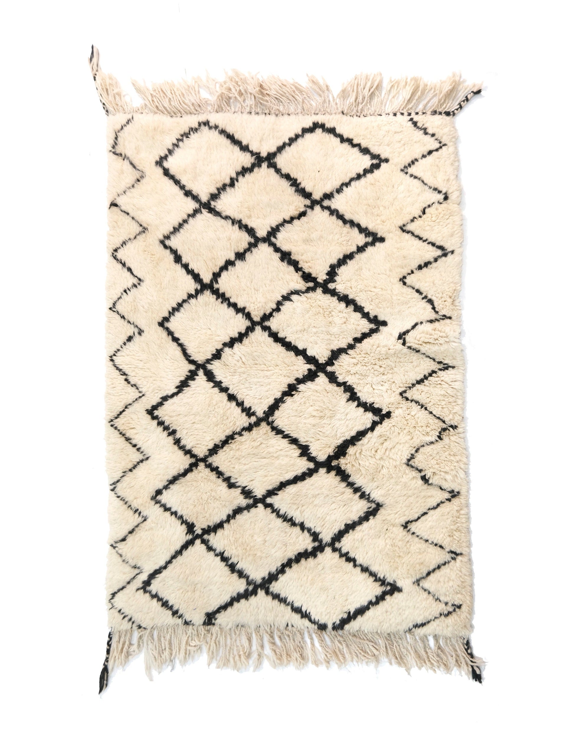 A cream-colored handwoven Moroccan shag rug featuring a central black diamond trellis pattern and zigzag side borders, with fringed edges detailed with black corner accents on the top and bottom.


