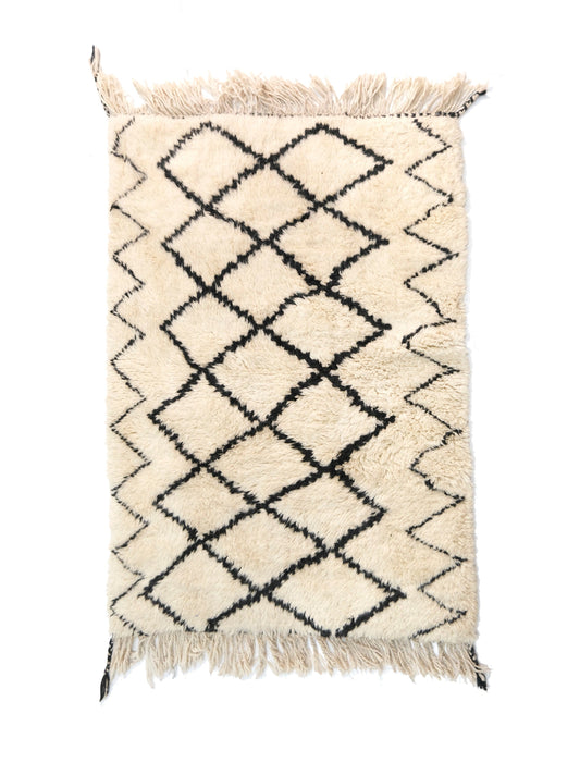 A cream-colored handwoven Moroccan shag rug featuring a central black diamond trellis pattern and zigzag side borders, with fringed edges detailed with black corner accents on the top and bottom.



