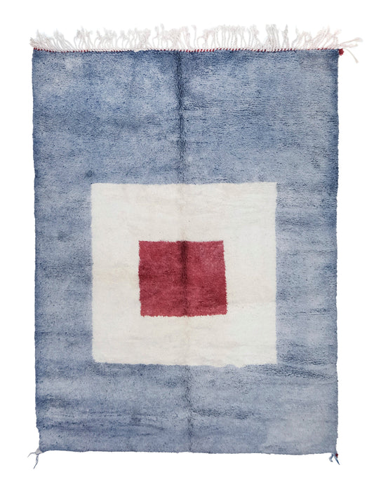 A plush handwoven Moroccan rug with a mottled light blue background, featuring a large white square in the center with a smaller red square inside it, finished with white fringe and red corner accents on the top and bottom edges.

