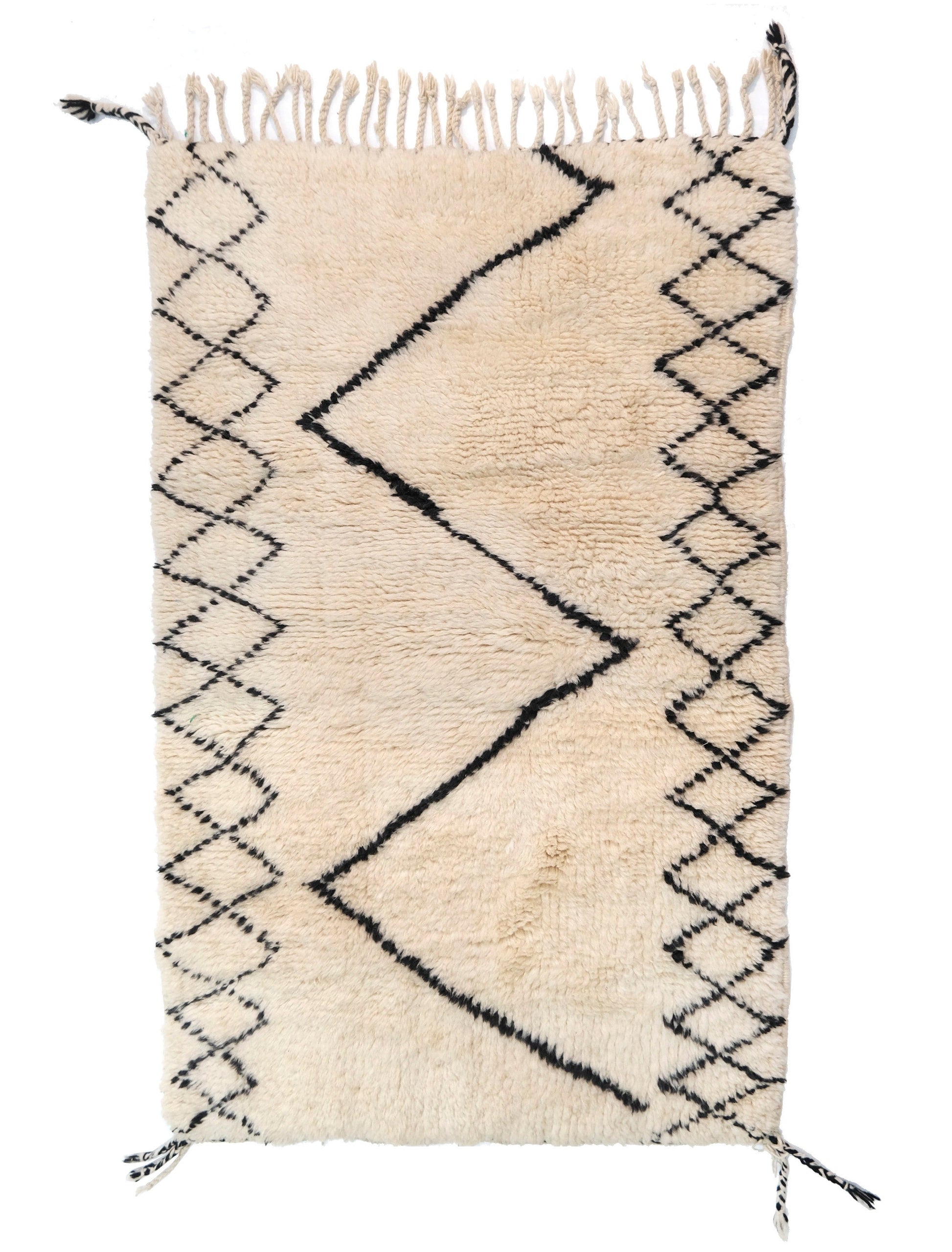 A cream-colored handwoven Moroccan shag rug featuring a bold, central black zigzag line flanked by black diamond lattice patterns on the sides, finished with cream fringe and black corner accents on the top and bottom edges.

