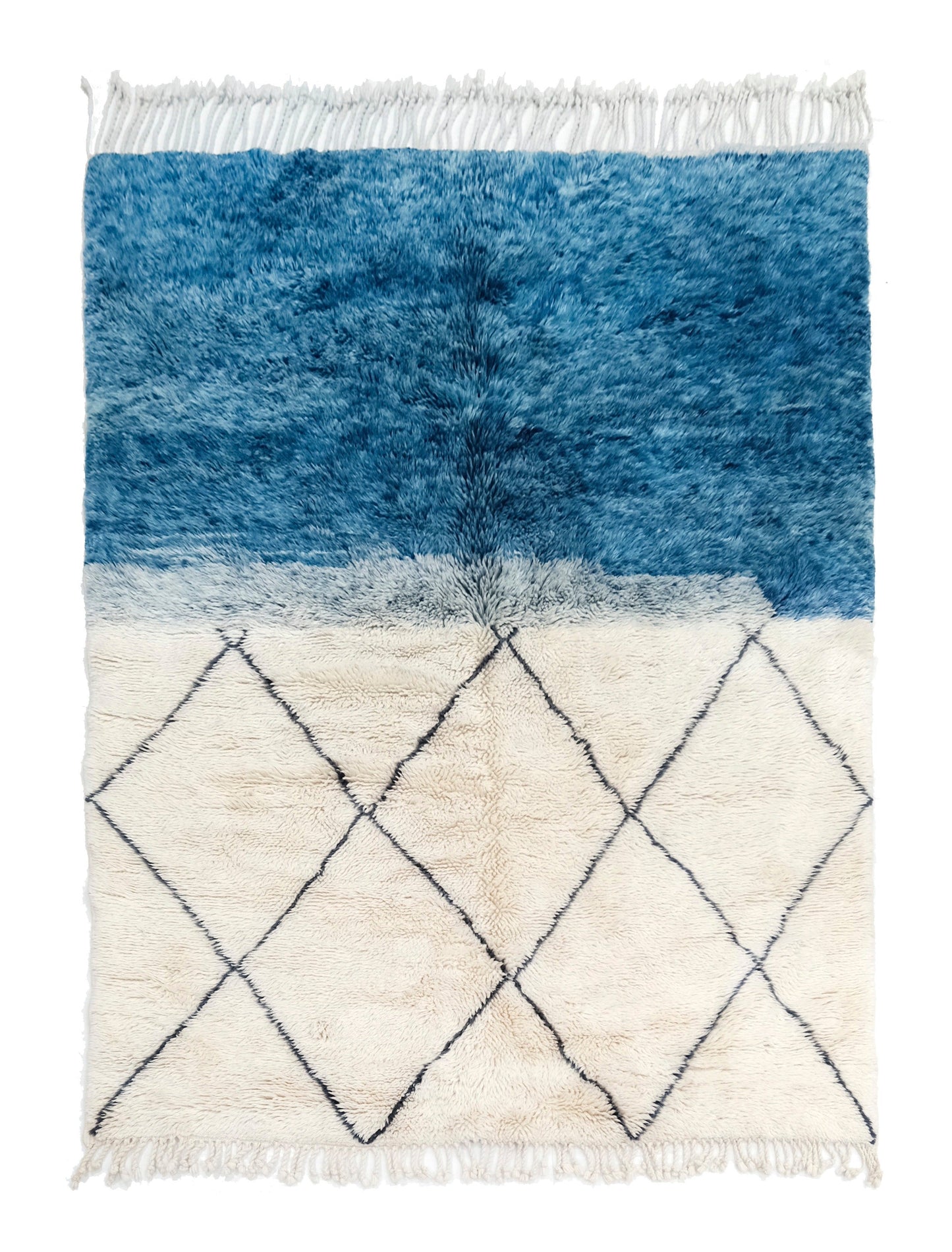 A handwoven Moroccan shag rug featuring a blue color-block top section blending into a cream bottom section with a black diamond trellis pattern, finished with white fringe on the top and bottom edges.

