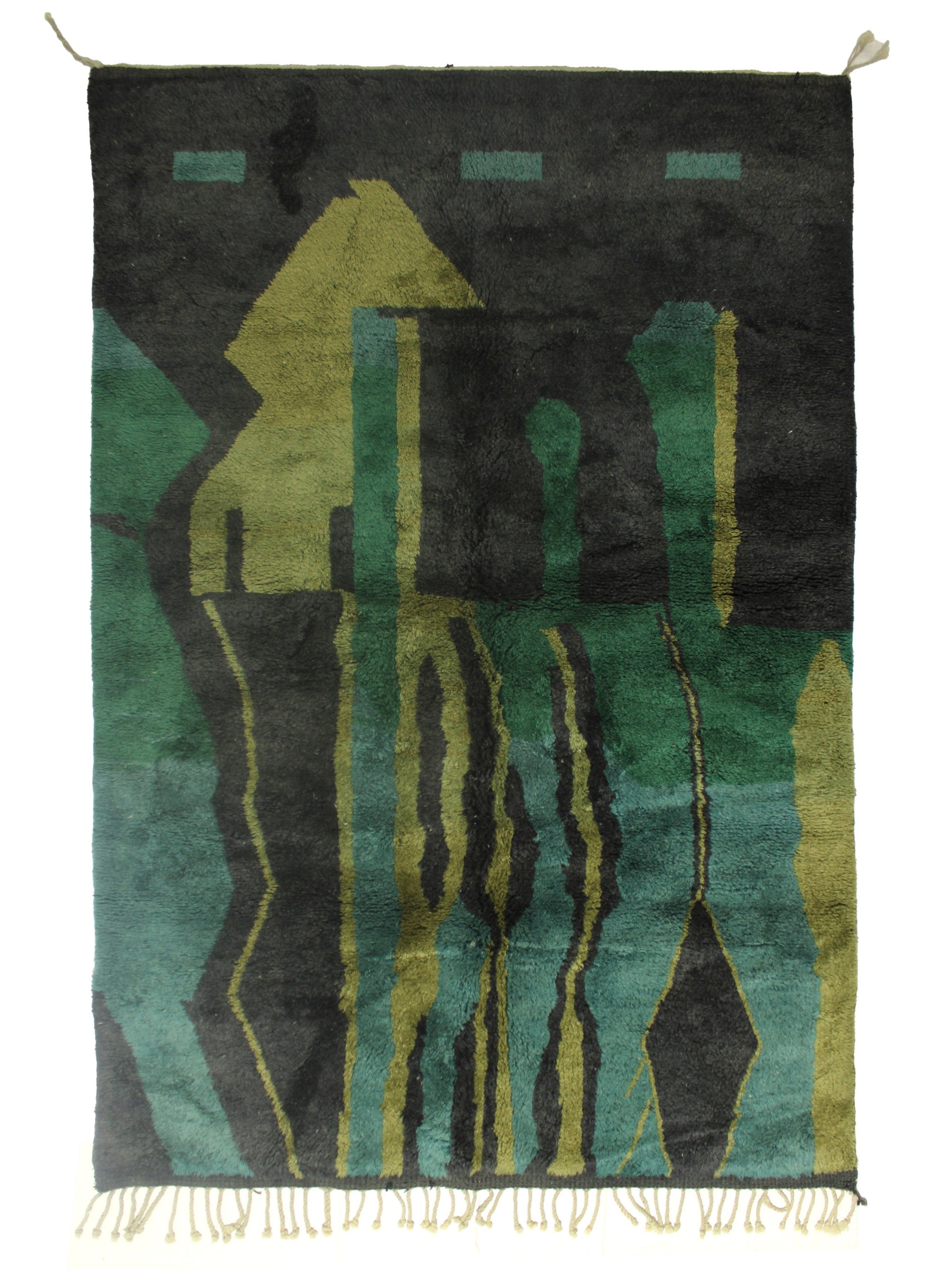 A dark charcoal Moroccan shag rug featuring bold abstract shapes in emerald green, teal, and chartreuse, with vertical wavy lines and geometric motifs, finished with cream fringe on the bottom edge and corner ties at the top.

