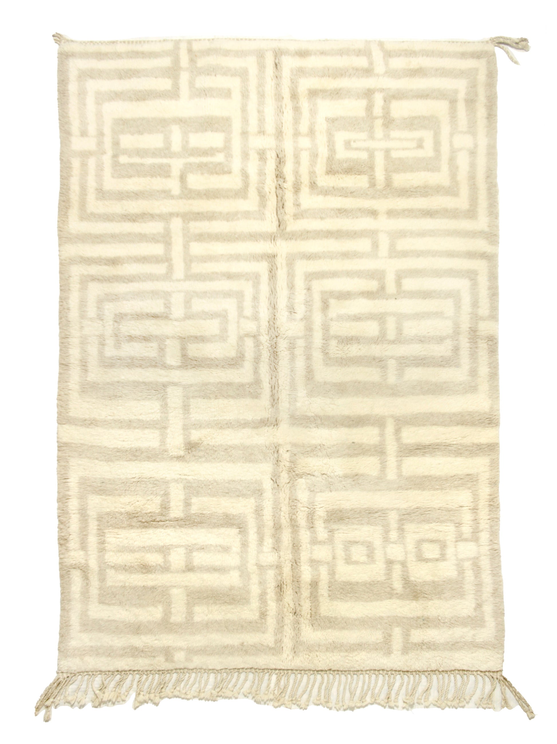 
A cream-colored handwoven Moroccan shag rug featuring a large geometric beige maze or Greek key pattern arranged in a grid of six blocks, finished with fringe on the bottom edge and corner ties at the top.


