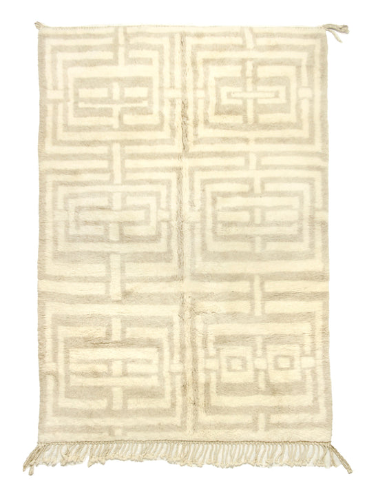 
A cream-colored handwoven Moroccan shag rug featuring a large geometric beige maze or Greek key pattern arranged in a grid of six blocks, finished with fringe on the bottom edge and corner ties at the top.


